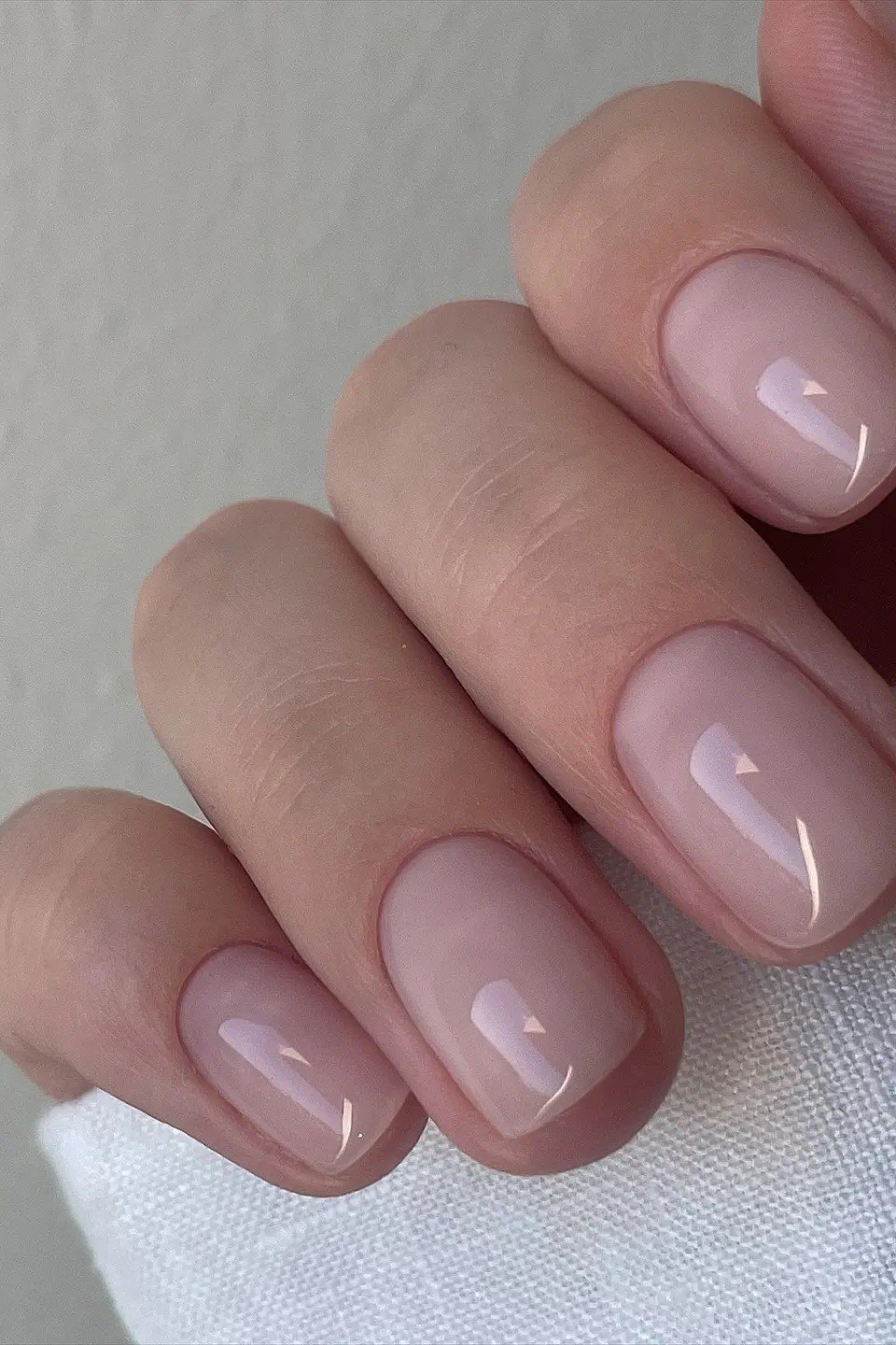 short squoval, glossy nude pink, side view of one hand on light fabric , for women over 60