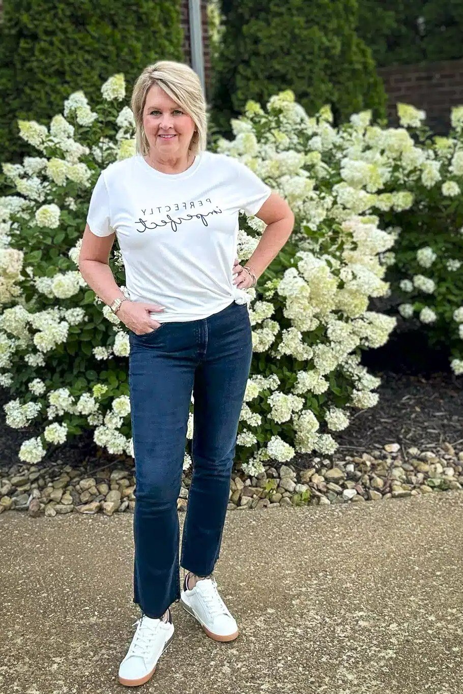 Woman over 50 wearing white graphic tee with dark jeans, everyday casual outfit idea