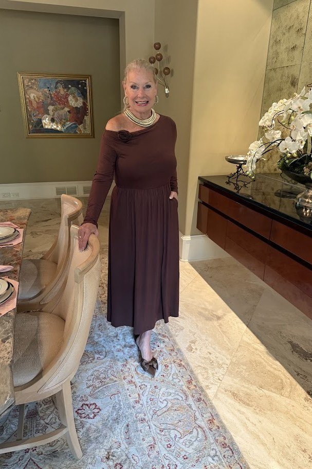 Older woman in burgundy off-shoulder maxi dress with layered gold necklaces