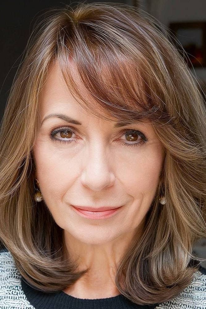 Medium layered haircut for women over 60 with wispy bangs, warm brown hair with highlights