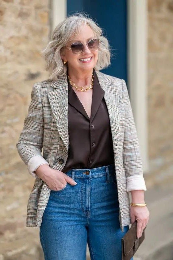 Woman over 60 wearing plaid blazer, black satin blouse, medium jeans, gold jewelry