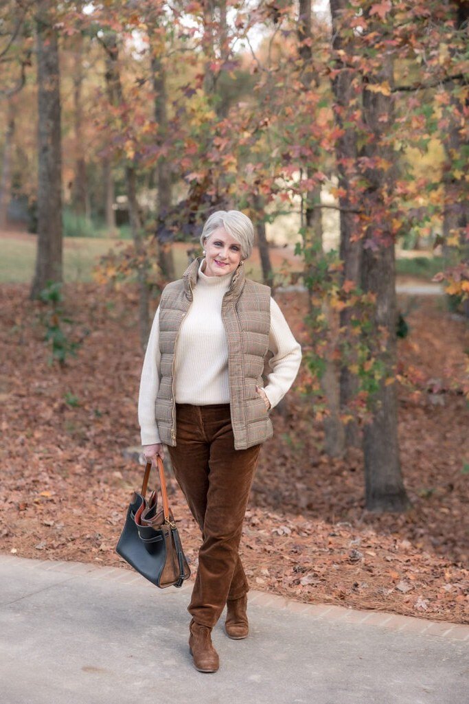 Fall city outfit for women over 50: cream puffer vest white top brown trousers, tote bag