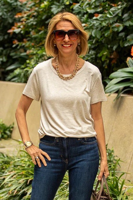 Woman over 50 wearing beige tee with dark jeans and gold necklace, everyday casual outfit idea