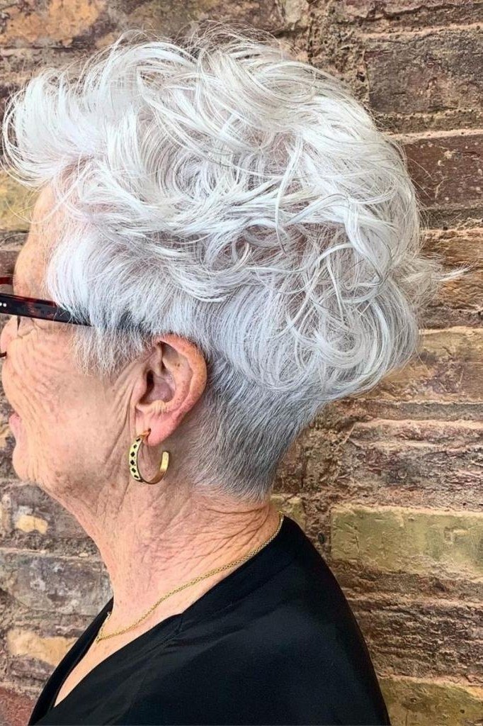 White curly pixie-bob side view, brick wall, glasses - curly hairstyle for women over 60