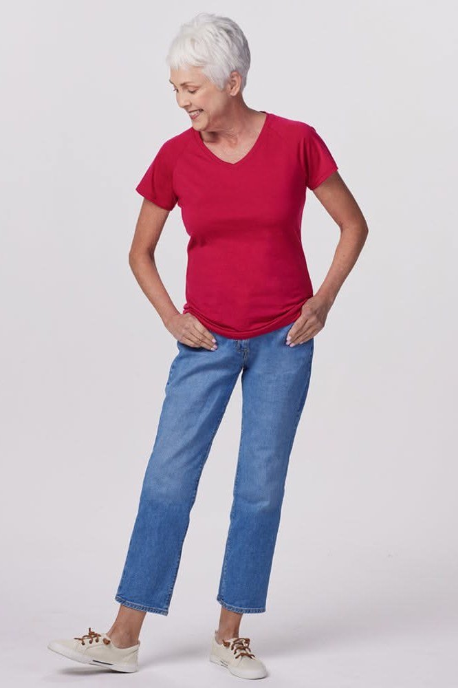 Woman over 50 wearing Red v-neck tee with straight blue jeans and sneakers, studio shot.