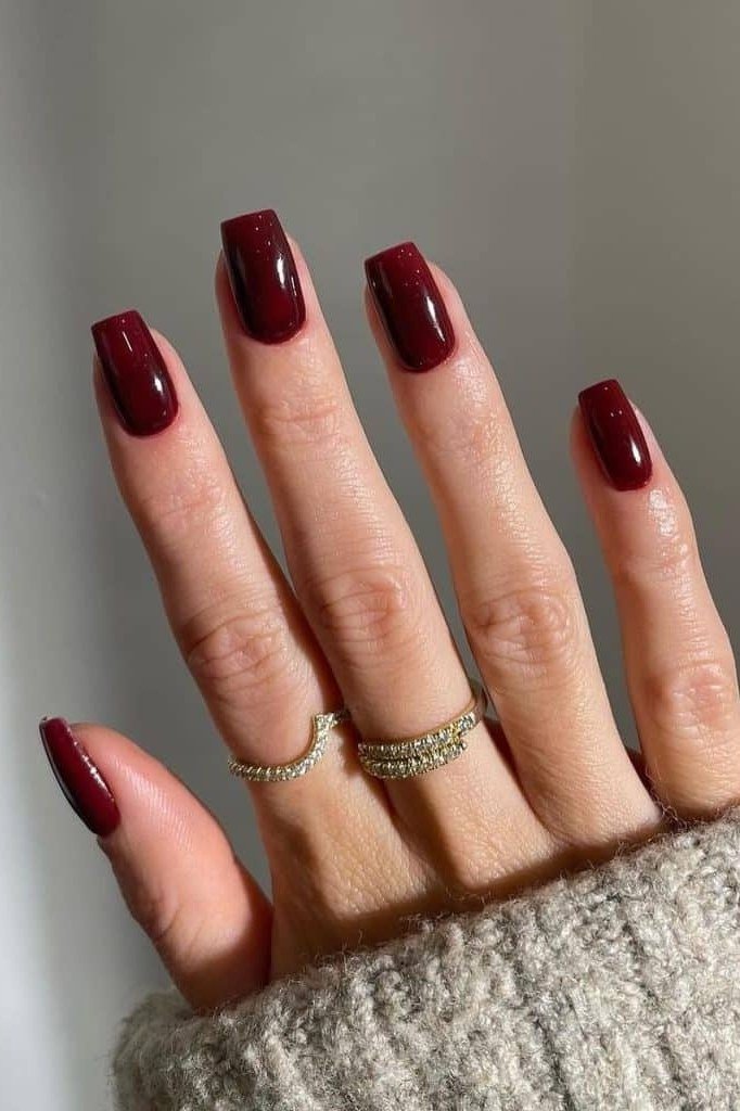 Deep burgundy short nails with gold rings, cream sweater, sophisticated nail design for women over 50