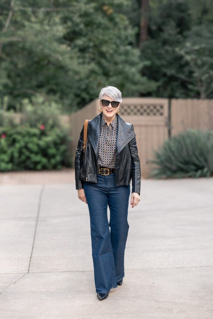 Fall city outfit for women over 50: black leather jacket blue jeans sunglasses walking