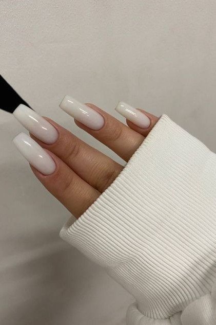 Milky white nails peeking from a cream sweater cuff