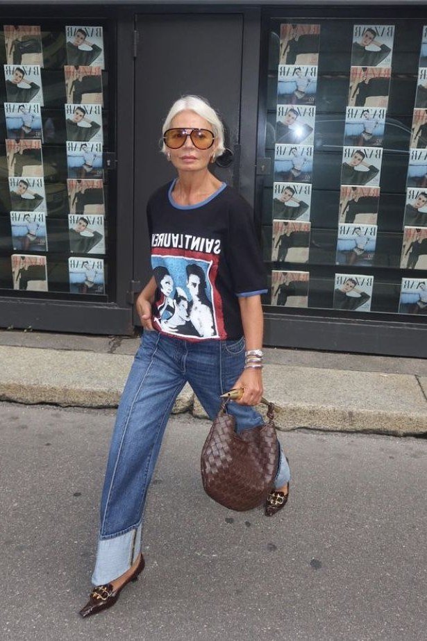 Woman over 50 wearing Graphic tee with cuffed jeans and sunglasses outside a storefront.