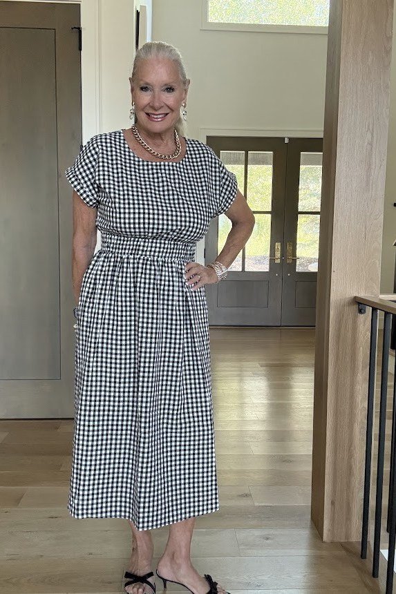 Older woman in a black-and-white gingham check midi shirt dress with a cinched waist, indoor hallway - summer dress for women over 50