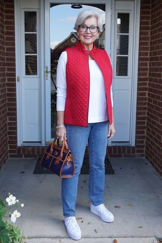 Red quilted vest over a white top with blue jeans and white sneakers, fall weekend outfit for women over 40