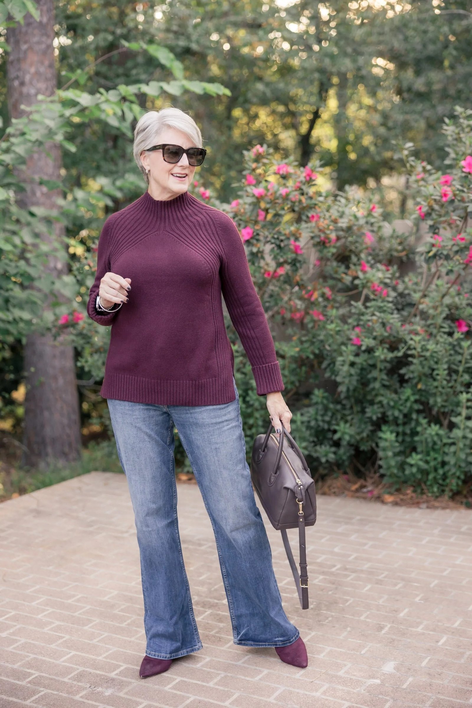 Woman over 50 wearing plum turtleneck sweater with relaxed blue jeans in garden