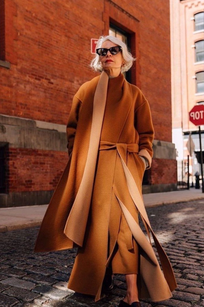 older woman in rust wrap coat with black turtleneck, city street