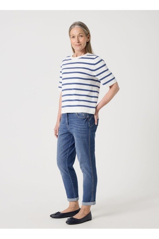 Woman over 50 wearing Navy and white striped tee with cropped jeans and flats, studio shot.