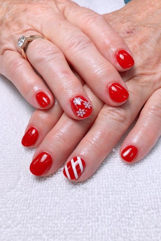 Elderly hands, bright red nails with snowflake and candy cane accents - classy Christmas nail idea for women over 70