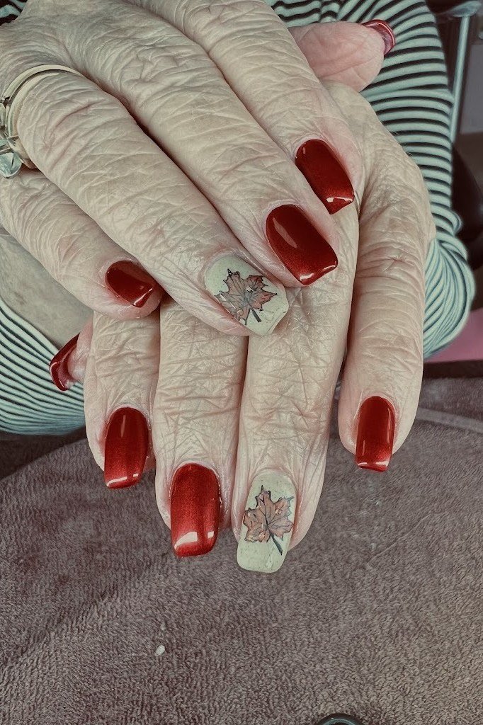 Deep red almond nails with delicate gold leaf nail art accents, elegant fall design.