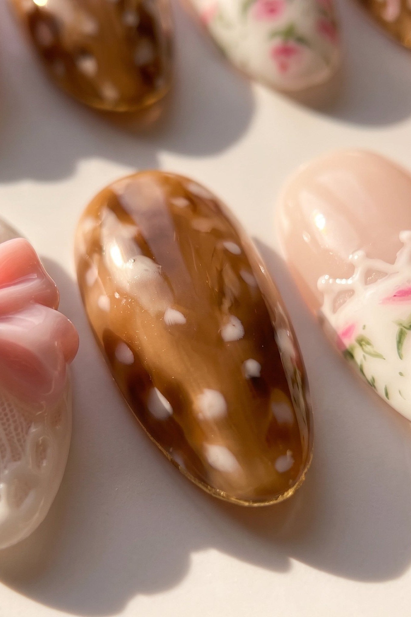 Extreme close-up of caramel brown almond nail with white fawn spots glossy