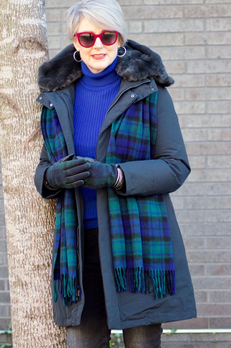 Stylish winter outfit for women over 60: navy plaid coat over blue turtleneck with gloves in falling snow