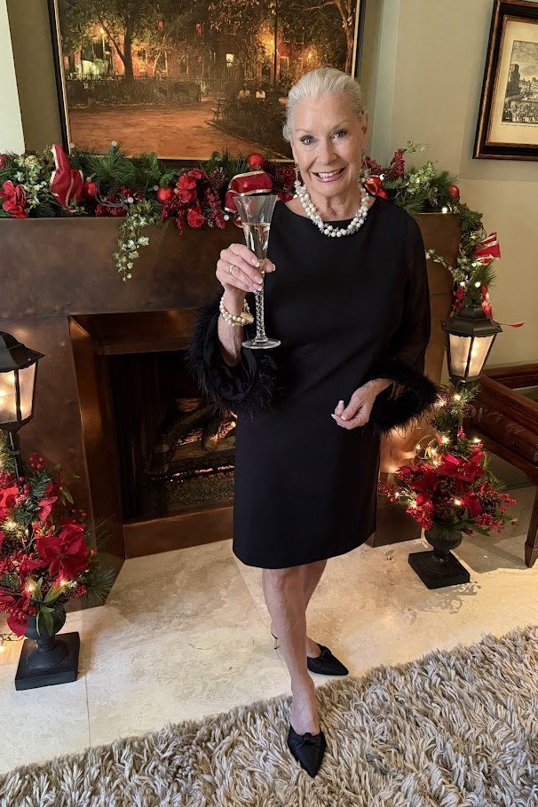holiday evening outfit for women over 60: black midi dress with fur cuffs at the fireplace