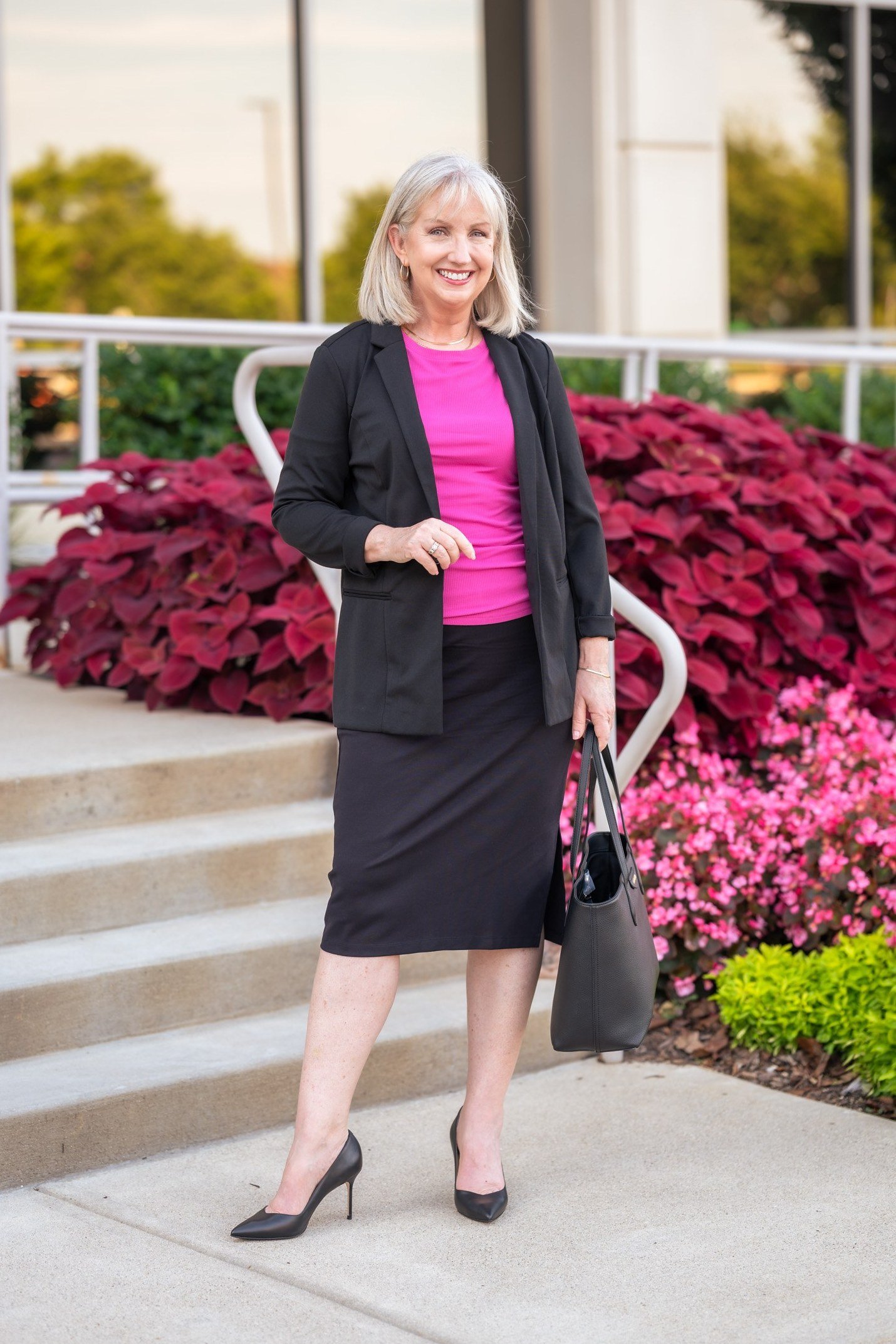 Woman over 50 in a hot pink blouse, black blazer and black pencil skirt