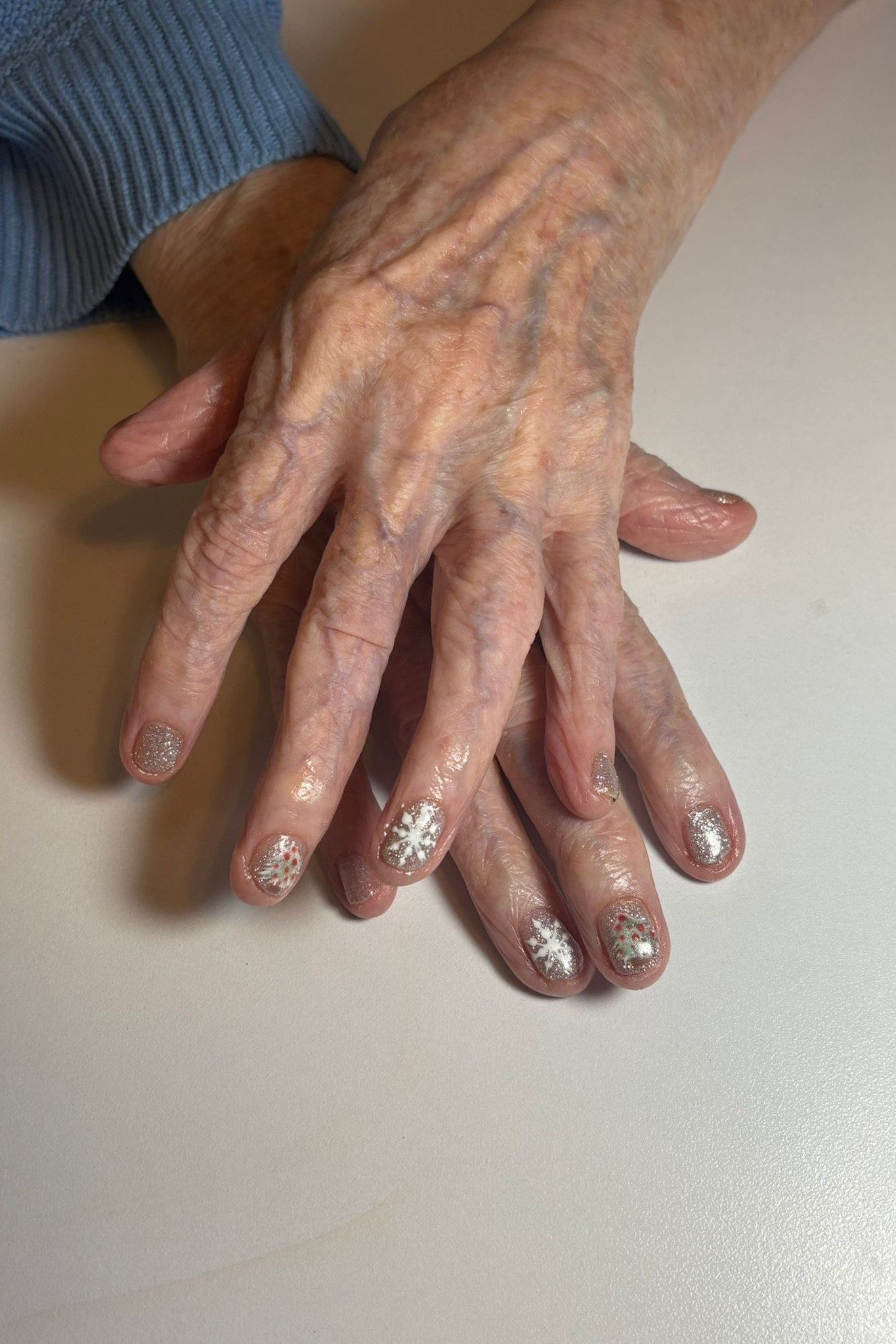 Elderly hands, neutral nails with subtle snowflake and silver art - classy Christmas nail idea for women over 70