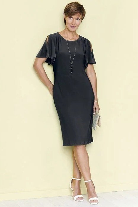 Black flutter-sleeve sheath dress, plain studio backdrop, chic night out outfit for women over 50