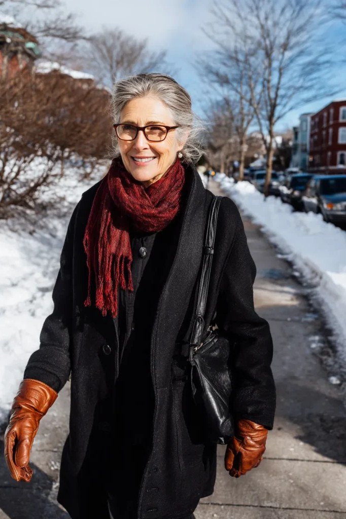 Stylish winter outfit for women over 60: black coat with red scarf and brown gloves in snow