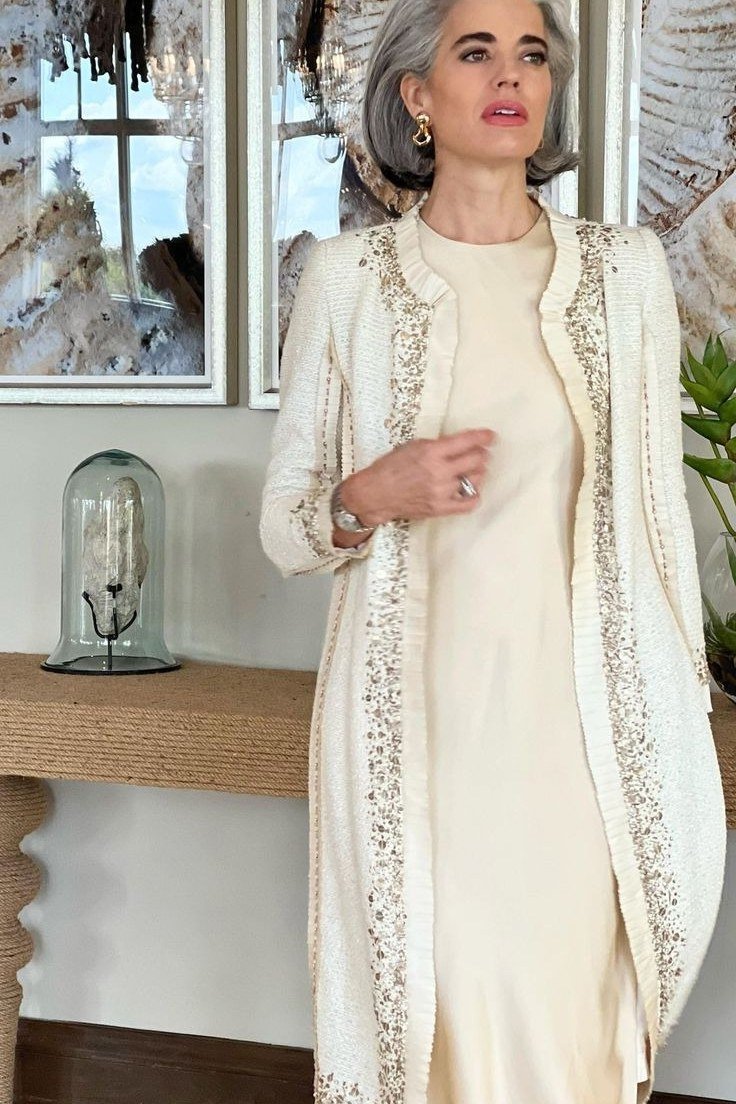 Silver-haired woman in ivory beaded long jacket over cream midi dress