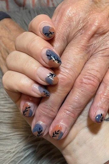 Slate grey-blue short nails with small autumn leaf nail art, glossy fall design on mature hands.