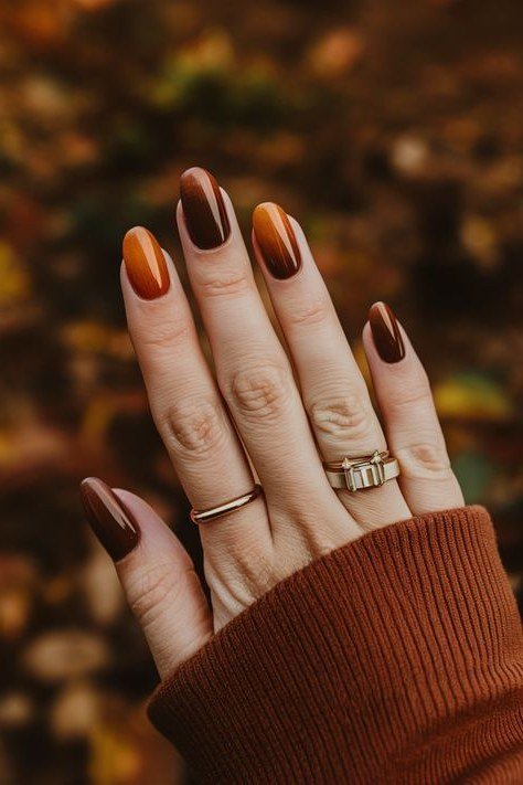 Pumpkin spice copper solid, almond shape, medium length, glossy, hand against blurred autumn leaves, fall nail color for women over 40