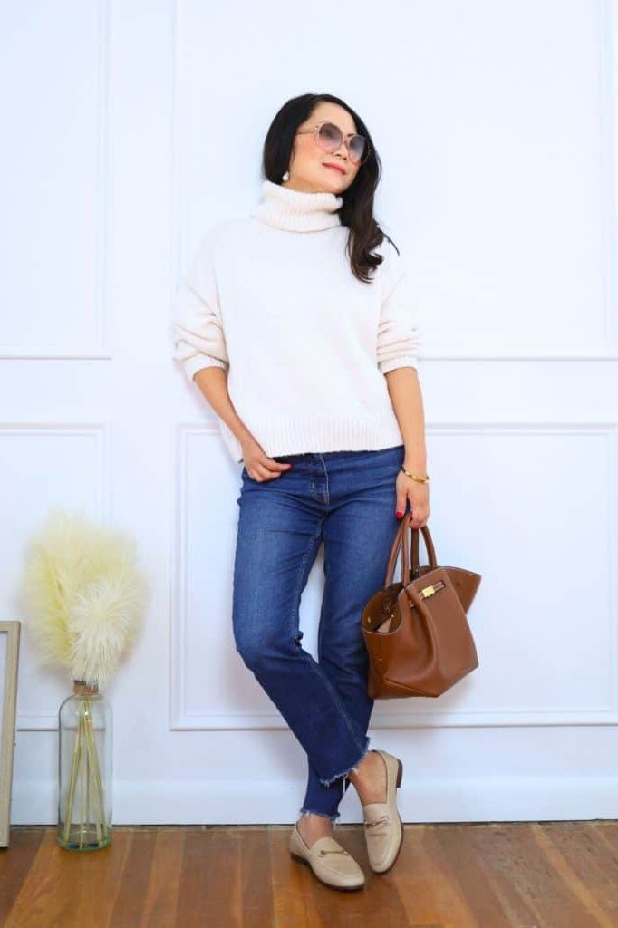 White turtleneck with blue jeans and tan bag, chic outfit for women over 40