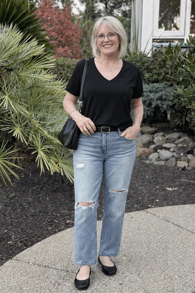 Woman over 50 wearing Black tee with ripped light-wash jeans and flats in a garden.