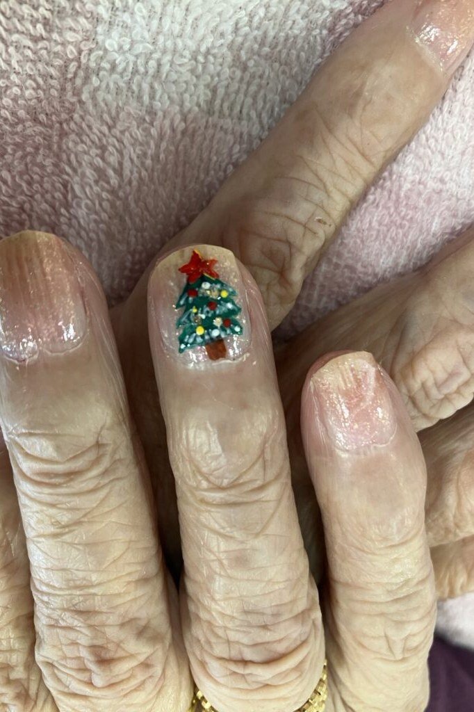 Natural nails with Christmas tree art on thumb, wrinkled hand - Christmas nail design for older women