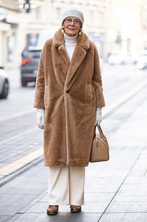 Stylish winter outfit for women over 60: camel teddy coat with cream turtleneck and white wide trousers