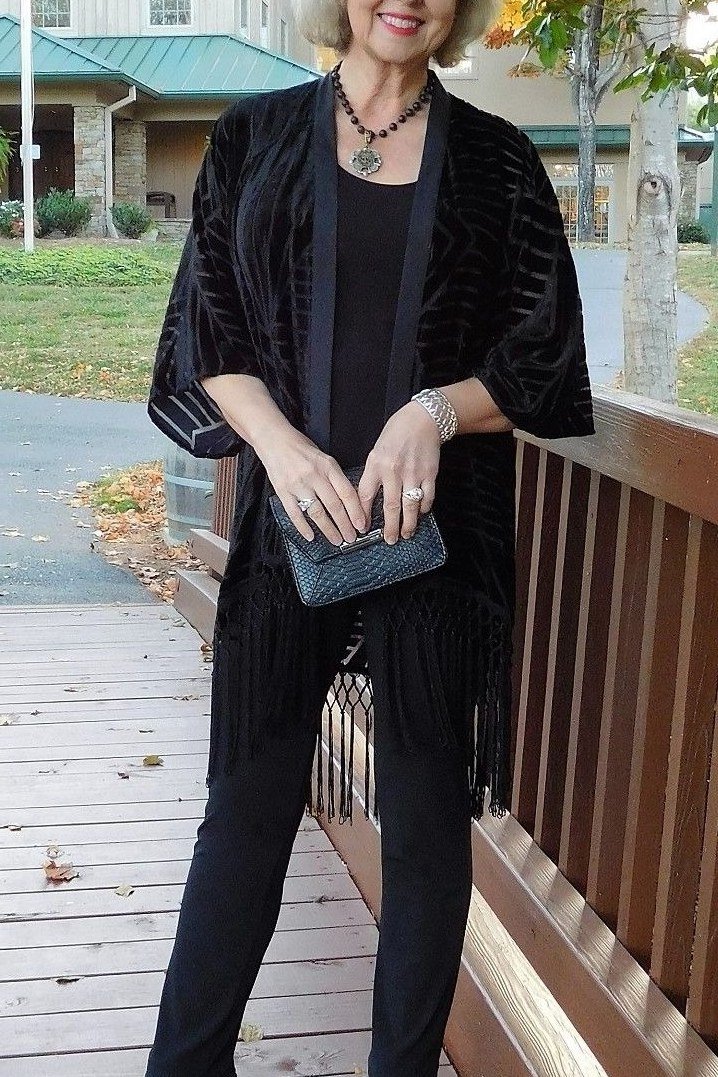 White-haired woman in black velvet jacket with black top and trousers and heeled boots on deck