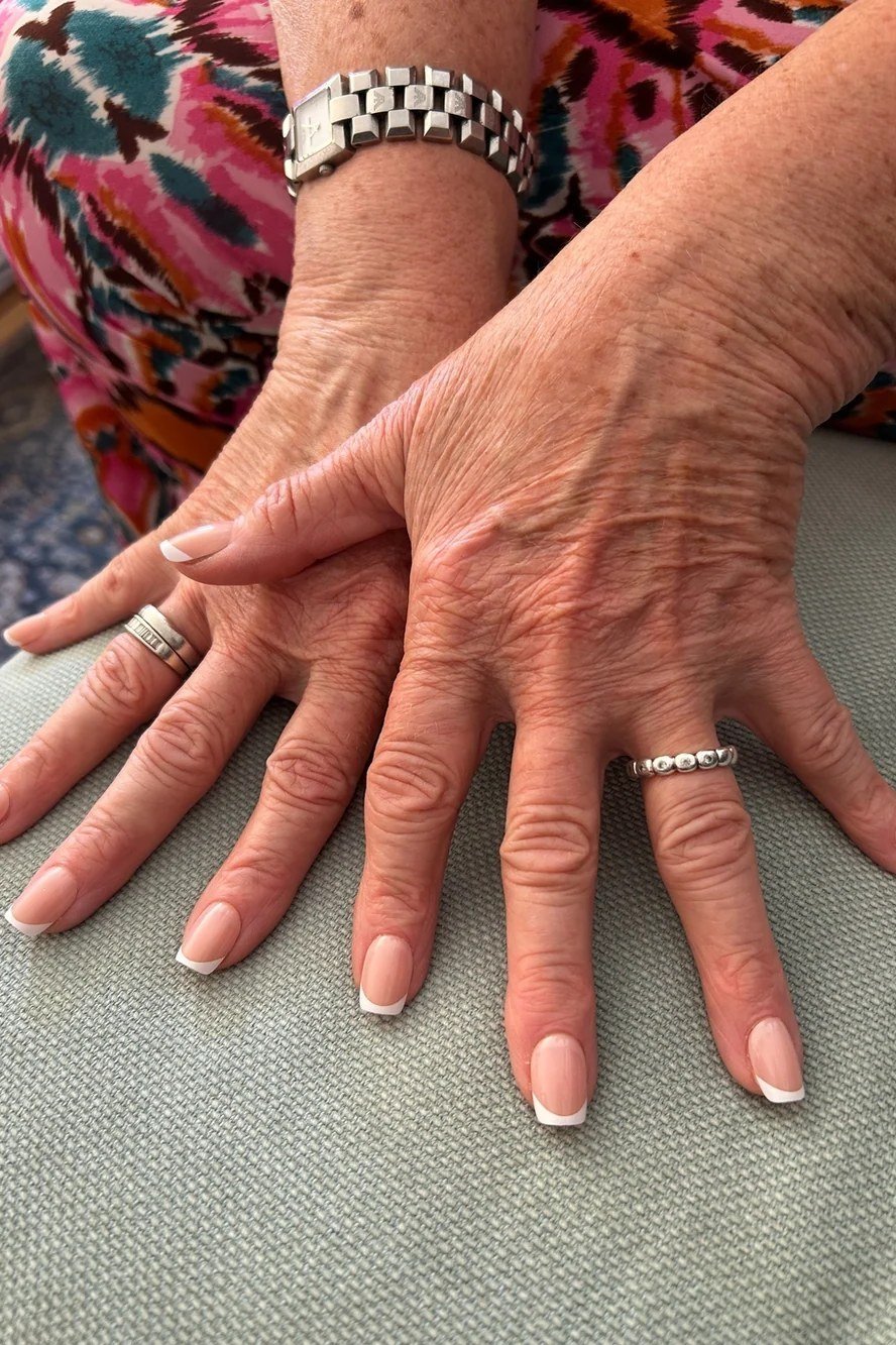 French manicure on mature hands with layered bracelets