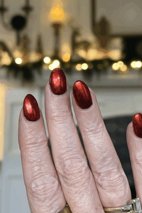 Deep burgundy red on mature hand, Christmas tree background - Christmas nail design for older women