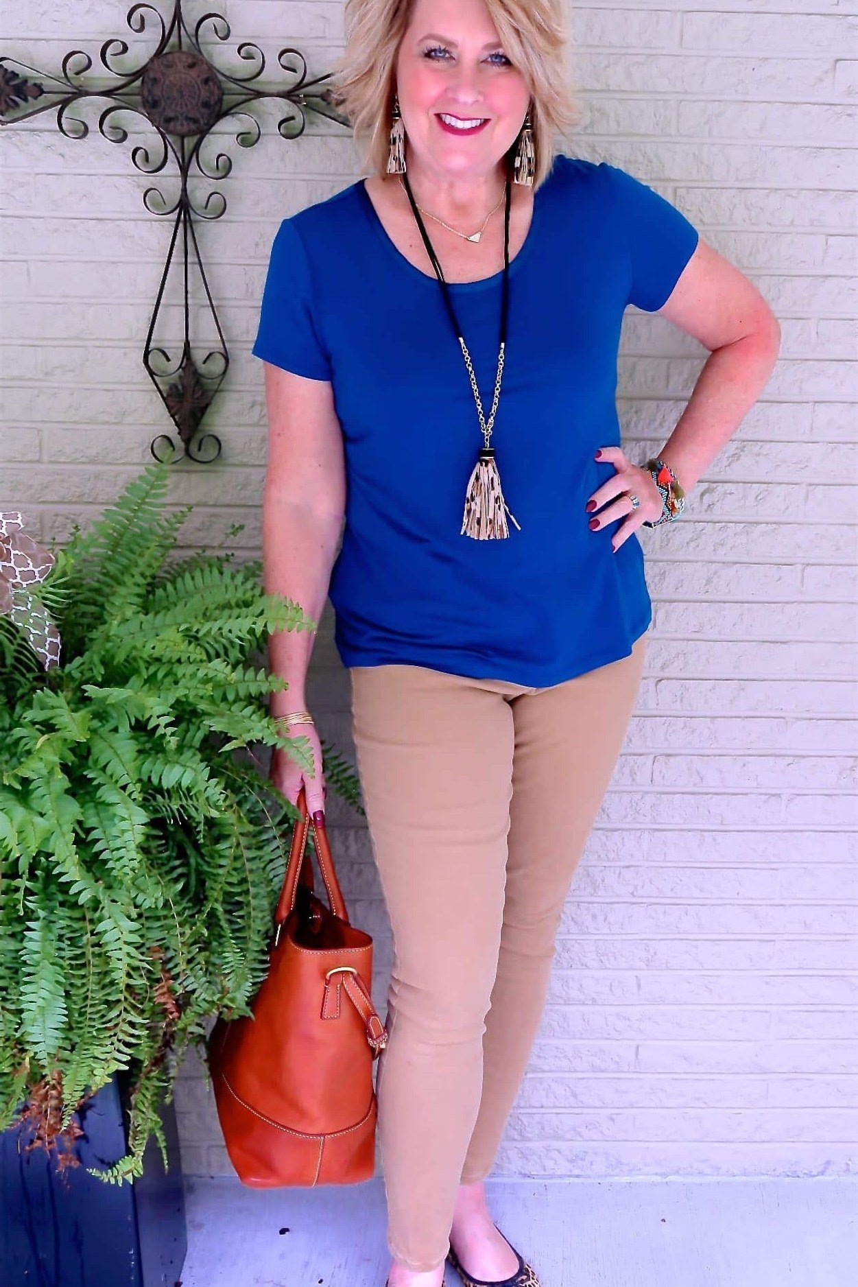 Woman over 50 wearing royal blue tee with beige pants and red tote, everyday casual outfit idea