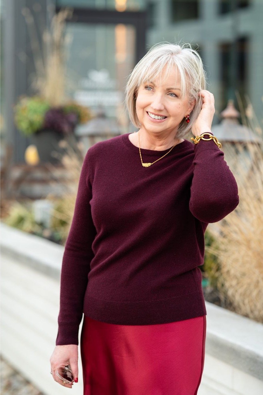 older woman in burgundy sweater with red satin midi skirt