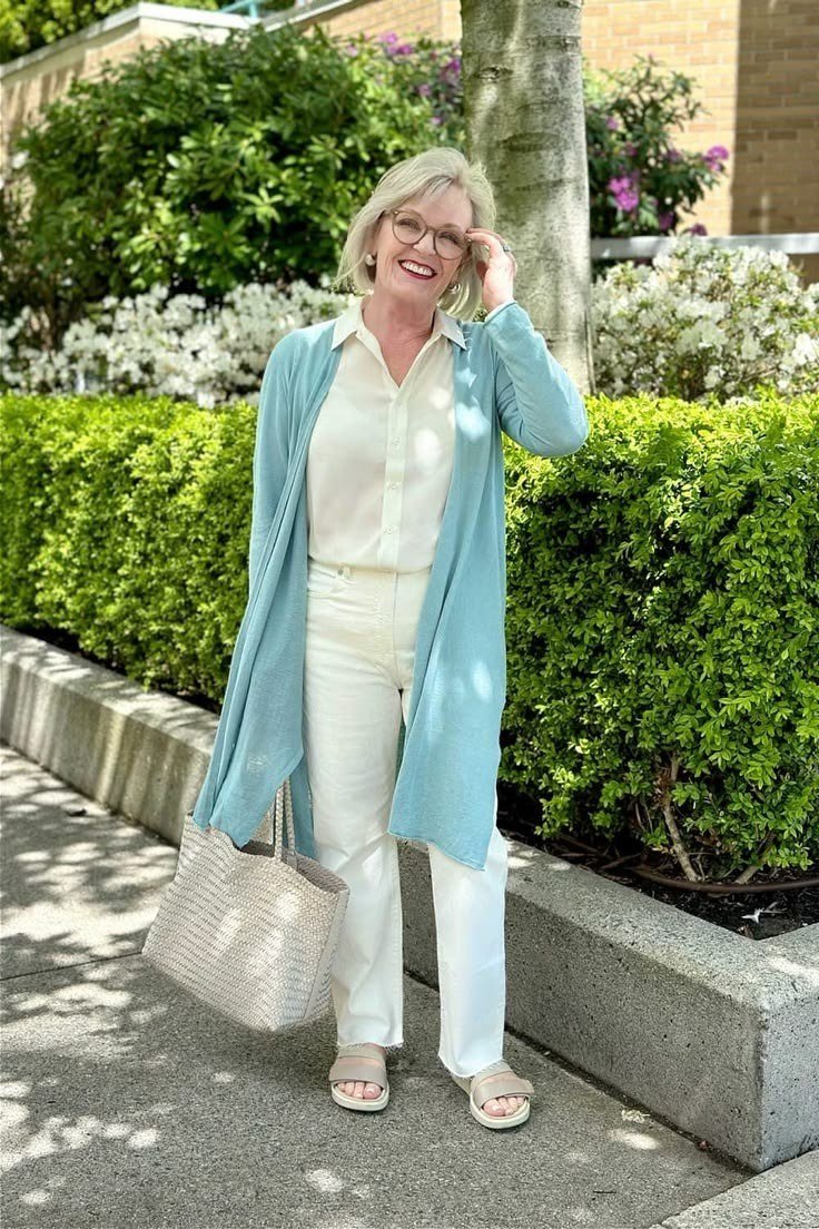 Woman over 60 in a light blue long cardigan over a white shirt and white trousers