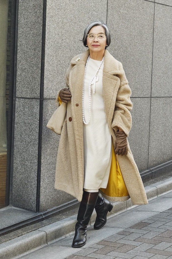 Stylish winter outfit for women over 60: camel coat over cream midi dress with brown knee boots