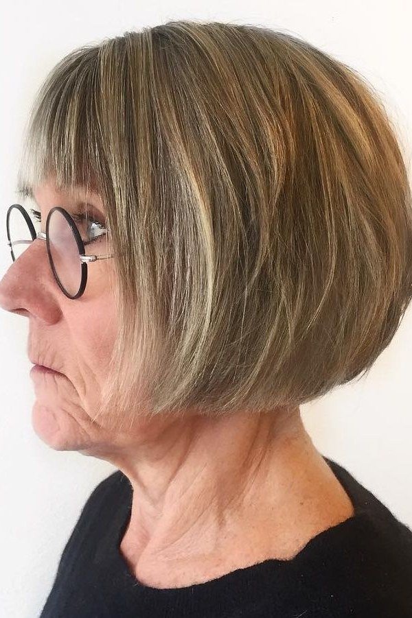 Brunette bob with full bangs and round glasses in profile for women over 60