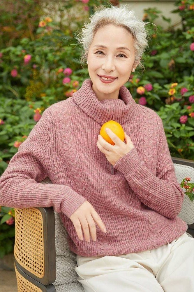 Rose-pink cable-knit turtleneck sweater holding an orange outdoors, cozy sweater outfit idea for women over 70