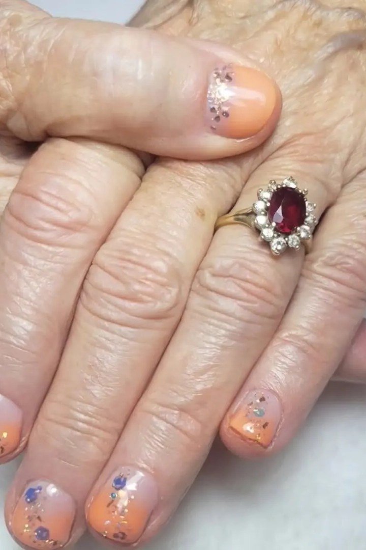 Peachy nude nails with subtle glitter on mature hands, fall nail design for older women