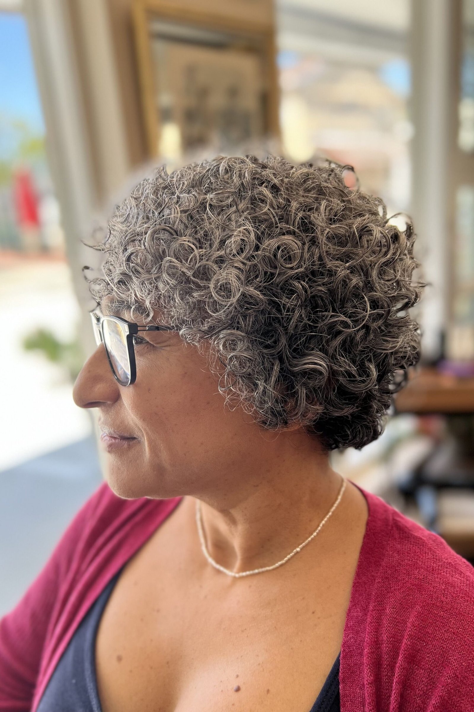 Grey tight curly bixie haircut side view with glasses for women over 60