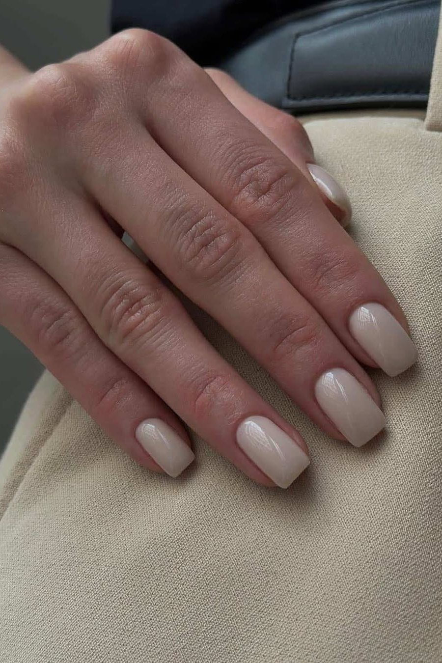 Milky nude nails resting softly on beige fabric
