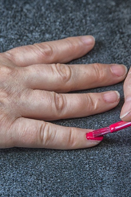 Applying thin coats of red nail polish on mature nails