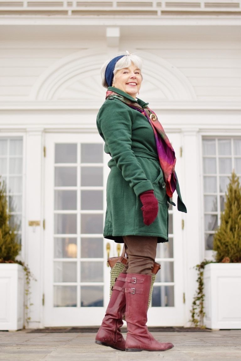 Stylish winter outfit for women over 60: green coat with red knee boots and knit beanie on steps