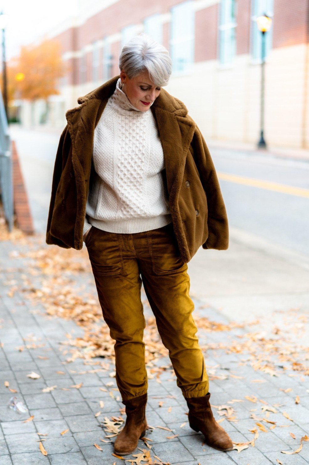 Brown corduroy jacket with cream cable knit turtleneck and mustard trousers