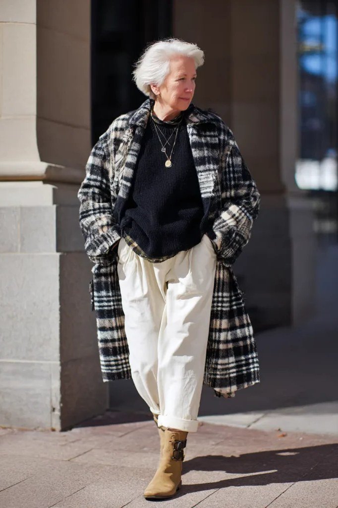 Stylish winter outfit for women over 60: black and white plaid coat with white cuffed pants and tan boots